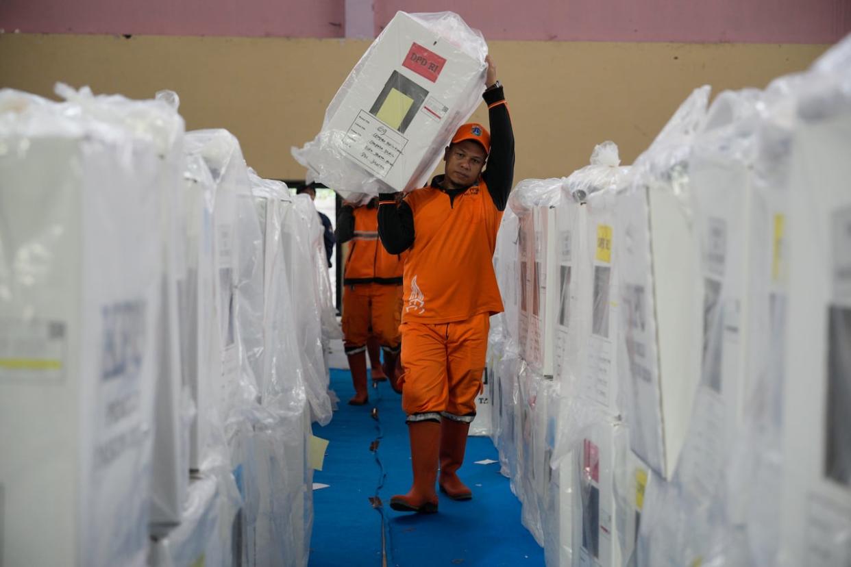 Workers carry ballot boxes prepared for Wednesday's election at a stadium in Jakarta, Indonesia, on Tuesday. Indonesia, the world's third-largest democracy, will open its polls on Wednesday to nearly 205 million eligible voters in presidential and legislative elections.  (Vincent Thian/The Associated Press - image credit)