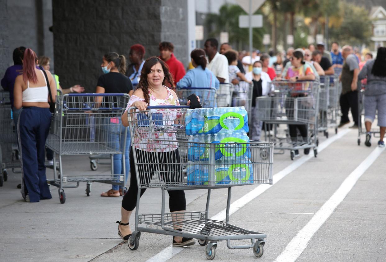 A long line of shoppers are seen past a person pushing cases of water outside a retail warehouse as people rush to prepare for Tropical Storm Ian in Kissimmee, Fla. on Sept. 25, 2022.