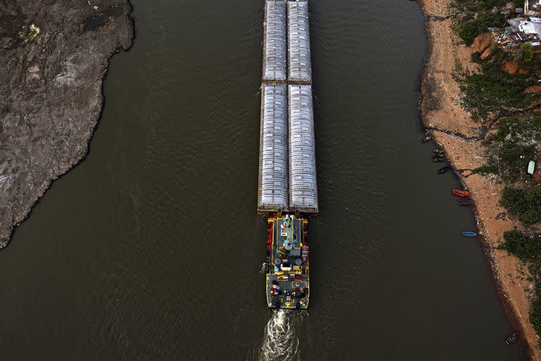 Barcazas cargadas de cemento navegan por el canal entre la playa y un antiguo volcán extinto, expuesto por el bajo nivel del río Paraguay, en Asunción, en medio de una histórica sequía que está afectando su nivel, el miércoles 22 de septiembre de 2021. (AP Foto/Jorge Saenz)