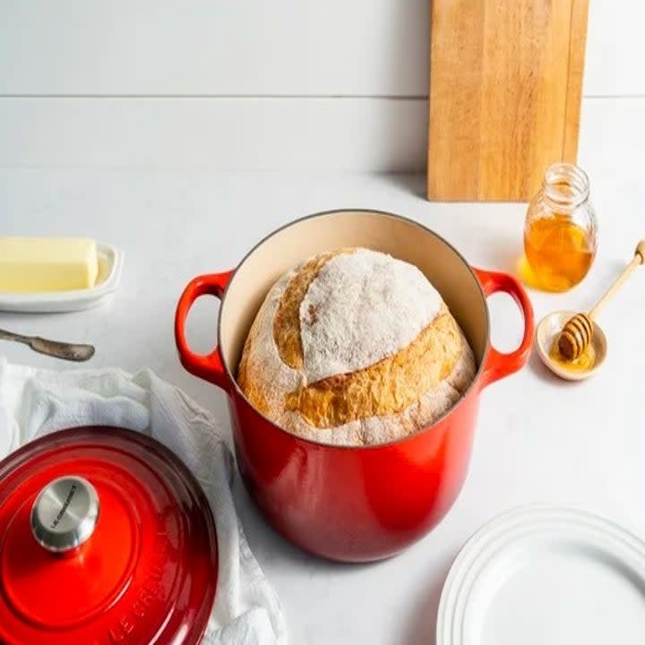 Red Dutch oven with baked bread inside it and lid next to it