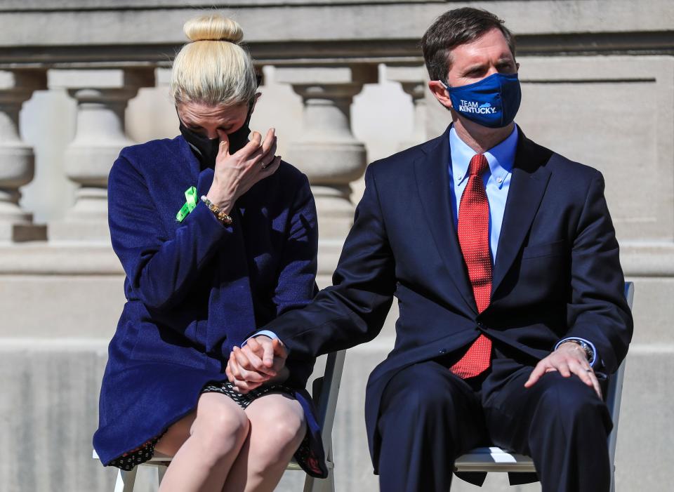 Kentucky first lady Britainy Beshear wipes away tears while holding her husband, Kentucky Gov. Andy Beshear, as they listen to family members who lost a loved one to COVID-19 during a memorial at the state Capitol in Frankfort on Saturday afternoon.