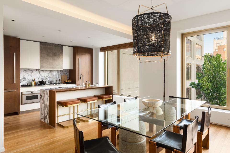 The open-plan kitchen and dining room is grounded by oak wood and accented in black and white. The stools at the oak bar are by Kravitz Design for CB2. A black pendant by Ay Illuminate hangs over the Giovanni Offredi for Saporiti dining table with chairs by Tobia and Afra Scarpa for Molteni. Kitchen appliances by Gaggenau.