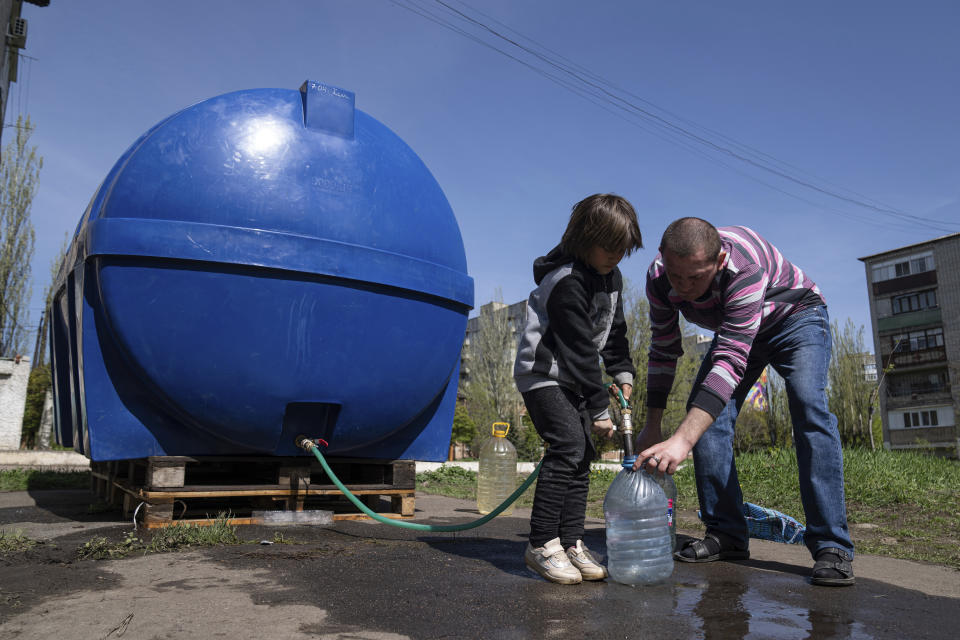 A girl Lisa helps a man to fill cans with water from a water tank installed for residents of Toretsk, eastern Ukraine, Monday, April 25, 2022. Toretsk residents have had no access to water for more than two months because of the war. (AP Photo/Evgeniy Maloletka)