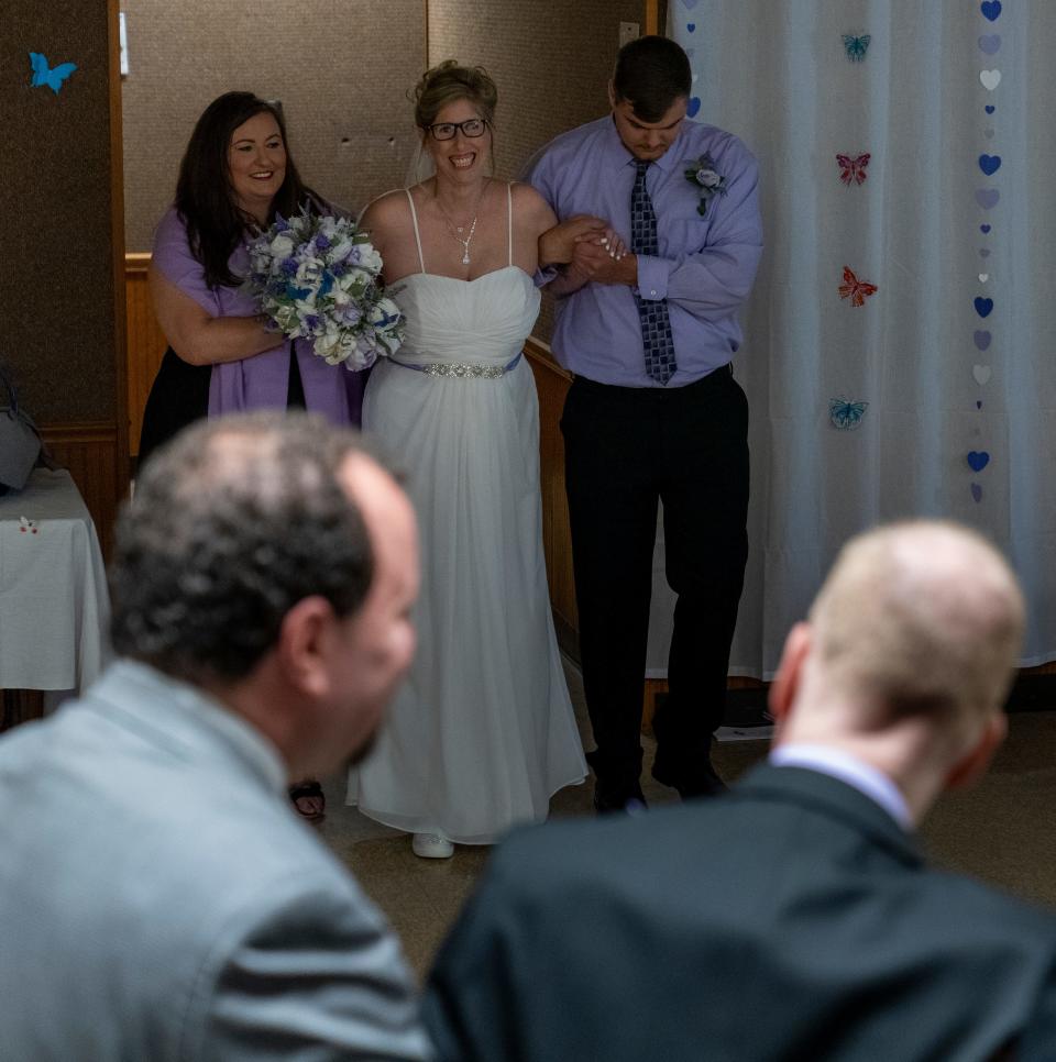 Sara Smouther, who typically uses a wheelchair, gets help walking into the room, Cloverdale, Ind., Saturday, May 21, 2022, during her wedding to Matt Weeks. The couple, who have the same inherited fatal disease, live in a Cloverdale community for Huntington’s patients. 