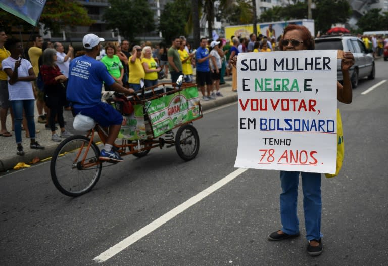 A 78-year-old black woman holds up a poster affirming that she will vote for Jair Bolsonaro in Sunday's election, despite his controversial stances