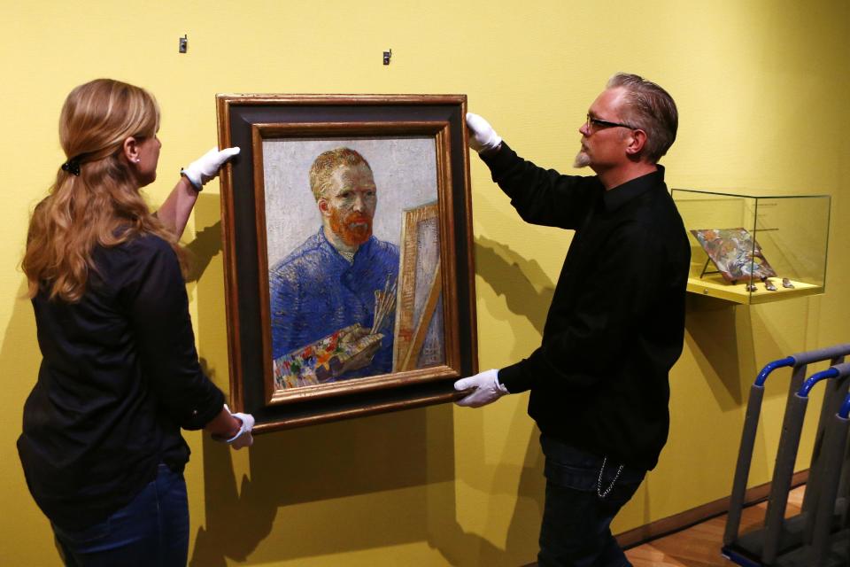 Curators hang an 1888 self-portrait of Vincent Van Gogh in which he painted himself behind a canvas, brushes and palette in hand, the final painting before the reopening after a seven-month renovation, at Van Gogh museum in Amsterdam, Netherlands, Wednesday, May 1, 2013. Displayed on the right are a wooden palette and paints that Van Gogh used in 1890. (AP Photo/Vincent Jannink)