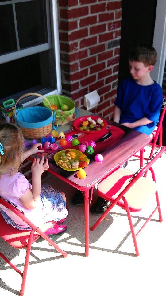 two children sitting at a red table eating lunch and playing with easter eggs