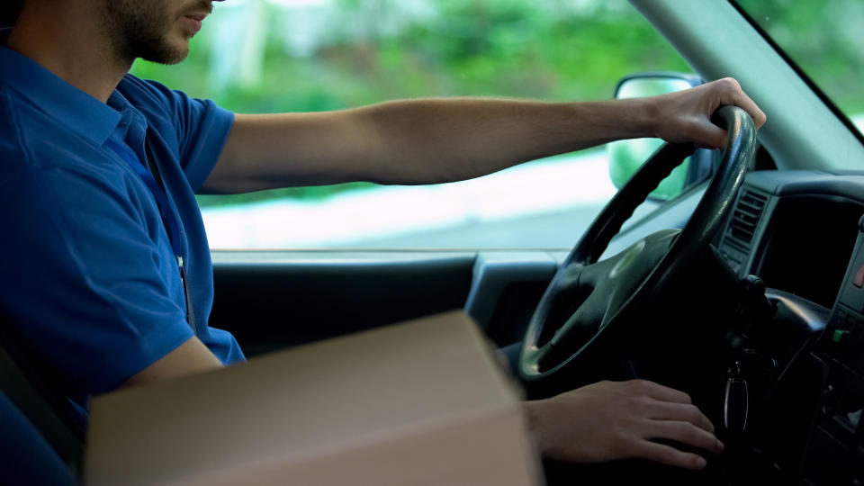 Mailman driving car, cardboard box standing near him, parcels express delivery