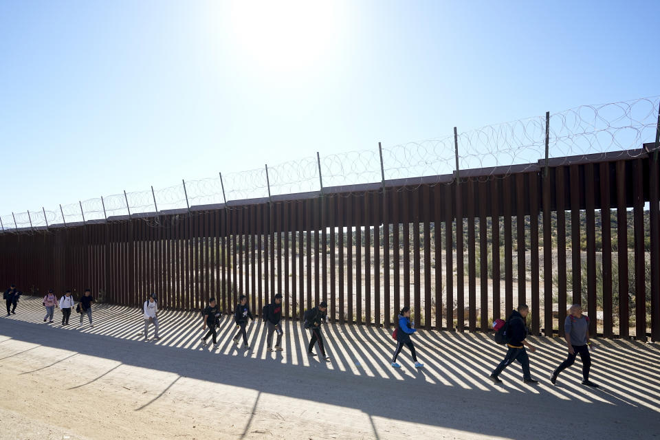 A group of people, including many from China, walk along the wall after crossing the border with Mexico to seek asylum, Tuesday, Oct. 24, 2023, near Jacumba, Calif. A major influx of Chinese migration to the United States on a relatively new and perilous route through Panama's Darién Gap jungle has become increasingly popular thanks to social media. (AP Photo/Gregory Bull)