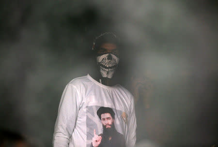 A man wearing a T-shirt with an image of Zakir Rashid Bhat also known as Zakir Musa, the leader of an al Qaeda affiliated militant group in Kashmir, as smoke billows from a room of a residential house that was damaged during a gun battle between Zakir and Indian security forces, in Dadasara village in south Kashmir's Tral May 24, 2019. REUTERS/Danish Ismail