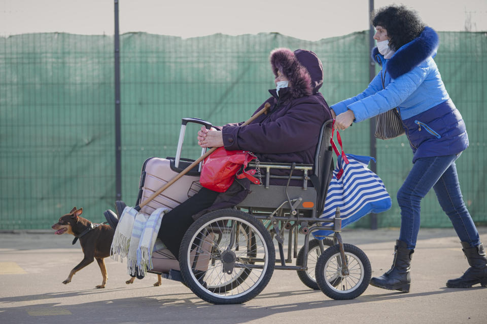 A woman pushes a wheelchair carrying an elderly lady from pro-Russian separatists controlled territory to Ukrainian government controlled areas in Stanytsia Luhanska, the only crossing point open daily, in the Luhansk region, eastern Ukraine, Tuesday, Feb. 22, 2022. Russian President Vladimir Putin has asked the country’s parliament for permission to use military force outside the country. That could presage a broader attack on Ukraine after the U.S. said an invasion was already underway there. (AP Photo/Vadim Ghirda)