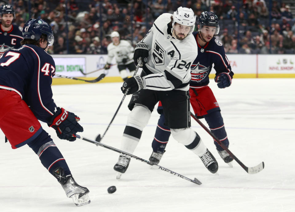 Los Angeles Kings forward Phillip Danault, center, shoots the puck between Columbus Blue Jackets defenseman Marcus Bjork, left, and forward Johnny Gaudreau during the first period of an NHL hockey game in Columbus, Ohio, Sunday, Dec. 11, 2022. (AP Photo/Paul Vernon)