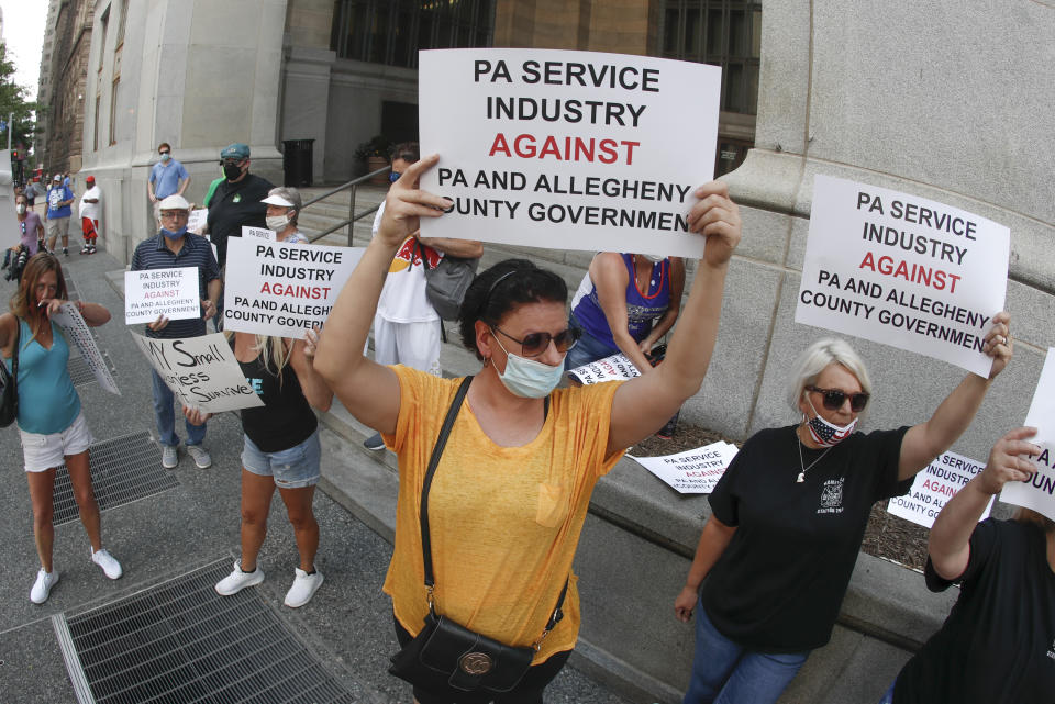 FILE - In this July 2, 2020, file photo, service Industry workers and supporters hold protest signs in front of Allegheny County offices in Pittsburgh. As coronavirus deaths soar, a growing number of restaurants in states across the country are reopening in defiance of strict COVID-19 rules that have shut them down for indoor dining for weeks, or even months. (AP Photo/Keith Srakocic, File)