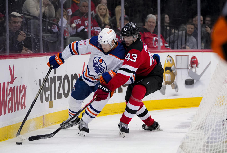 Edmonton Oilers left wing Warren Foegele (37) and New Jersey Devils defenseman Luke Hughes (43) vie for the puck during the first period of an NHL hockey game in Newark, N.J., Thursday, Dec. 21, 2023. (AP Photo/Peter K. Afriyie)