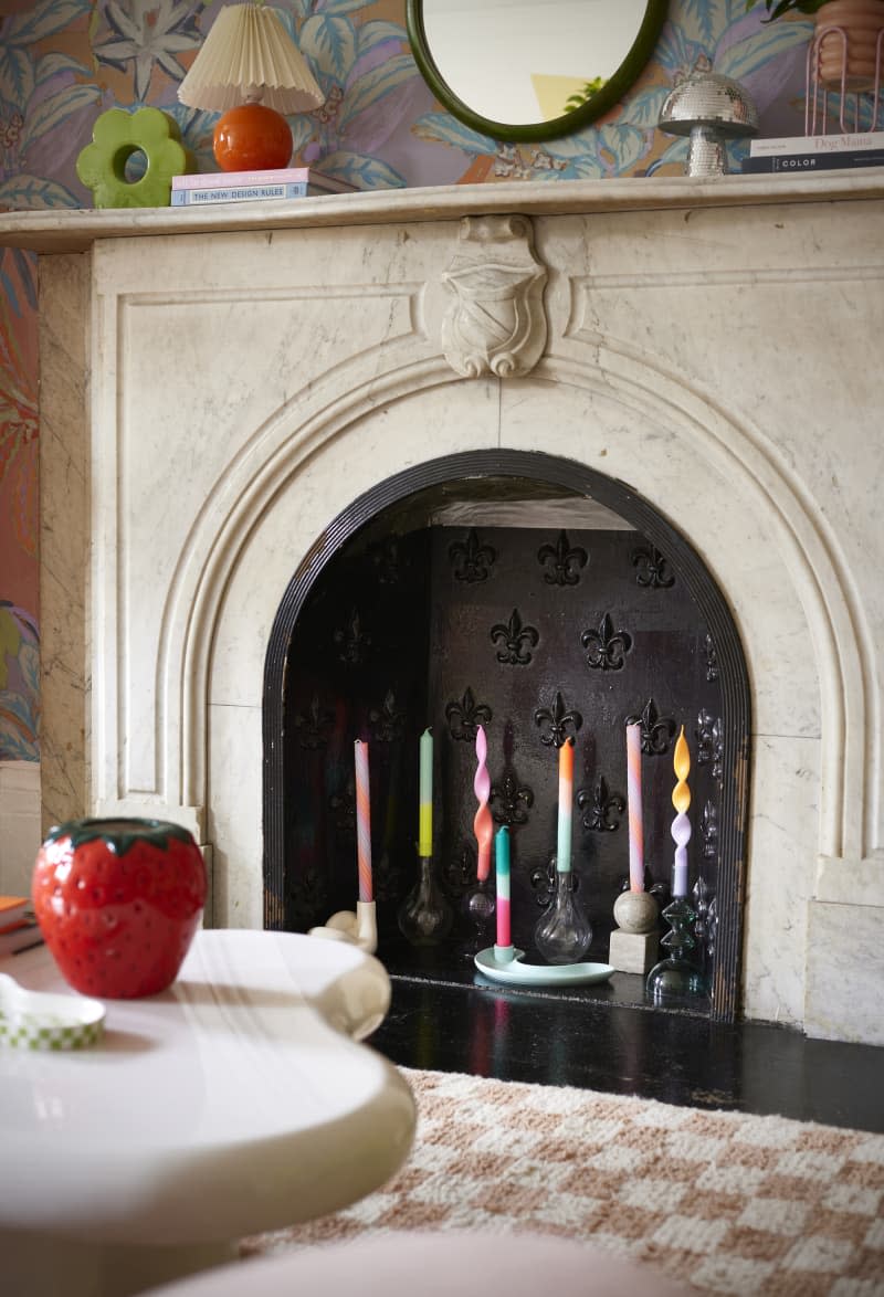 Colorful taper candles inside marble fireplace.