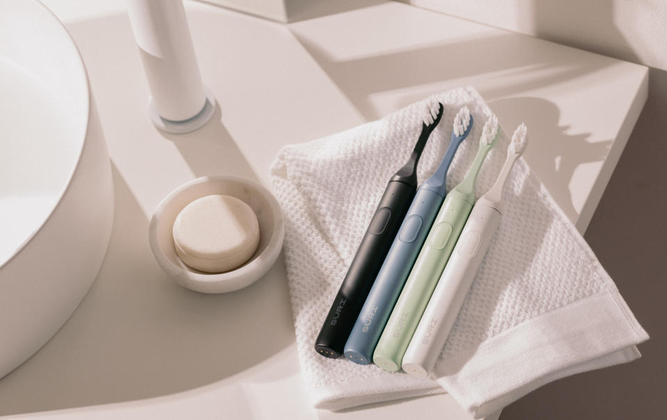 Four SURI Sonic toothbrushes rest on a towel on a sink.