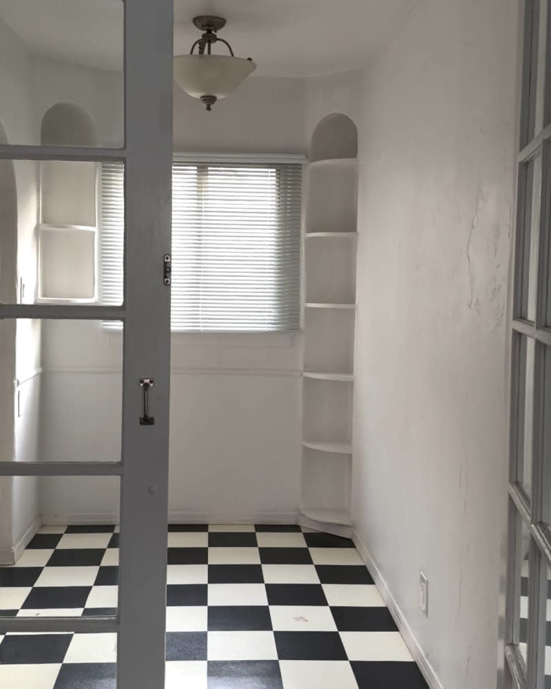 Black and white checkered tile floor, built in book case in corner, blinds on window, french doors with glass panels