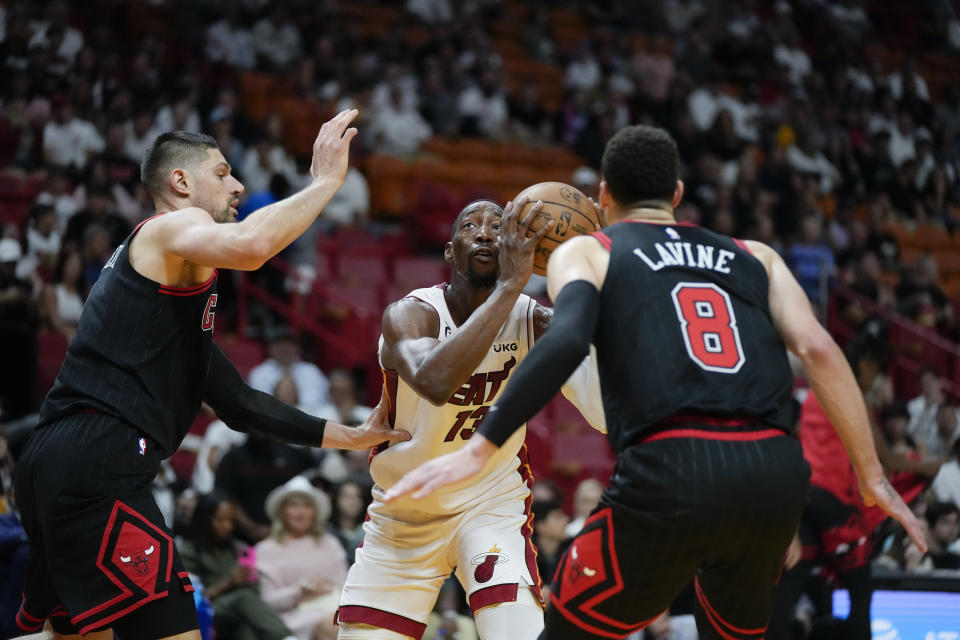 Miami Heat center Bam Adebayo (13) looks for an opening around the defense of Chicago Bulls center Nikola Vucevic, left, and guard Zach LaVine (8) during the first half of an NBA basketball play-in tournament game, Friday, April 14, 2023, in Miami. (AP Photo/Rebecca Blackwell)