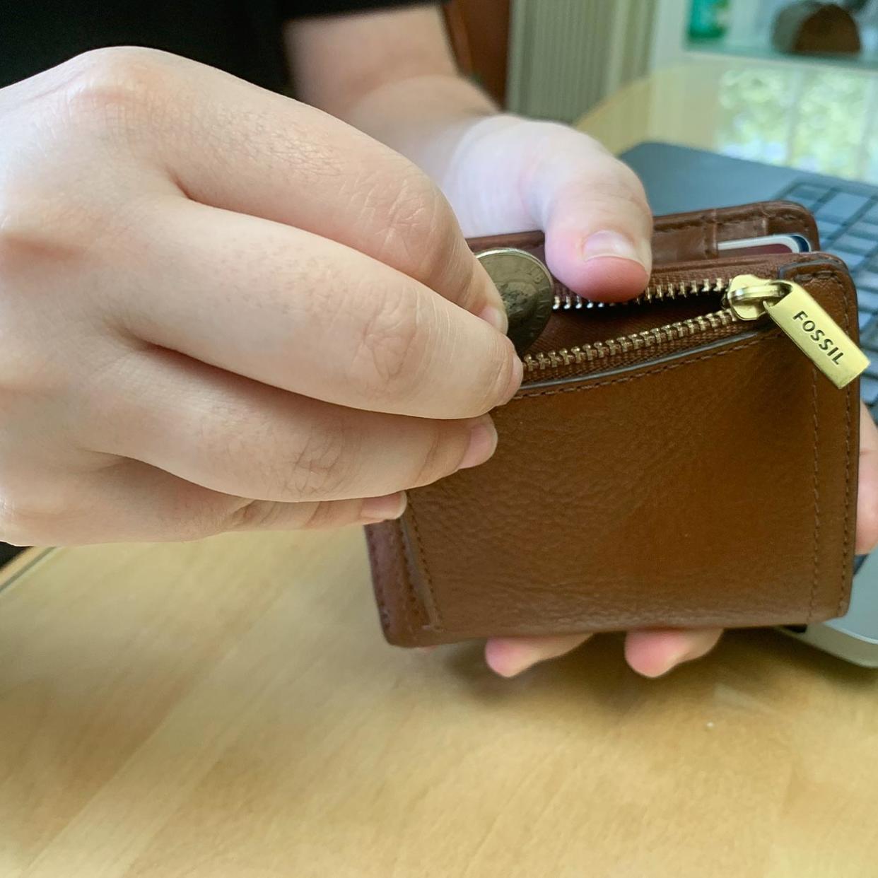 Image of someone adding change to the Logan Small RFID Bifold wallet (Courtesy Gabriella DePinho)