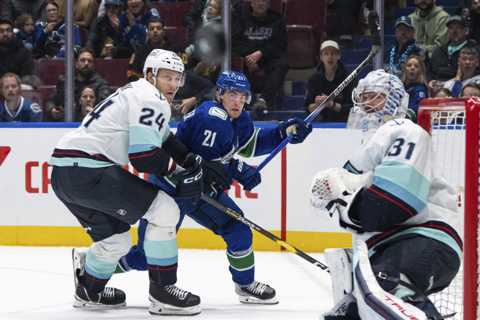 Seattle Kraken's Jamie Oleksiak (24) and Vancouver Canucks' Nils Hoglander (21) watch the puck after Seattle goaltender Philipp Grubauer (31) deflected a shot during the second period of an NHL hockey game Saturday, Nov. 18, 2023, in Vancouver, British Columbia. (Ethan Cairns/The Canadian Press via AP)