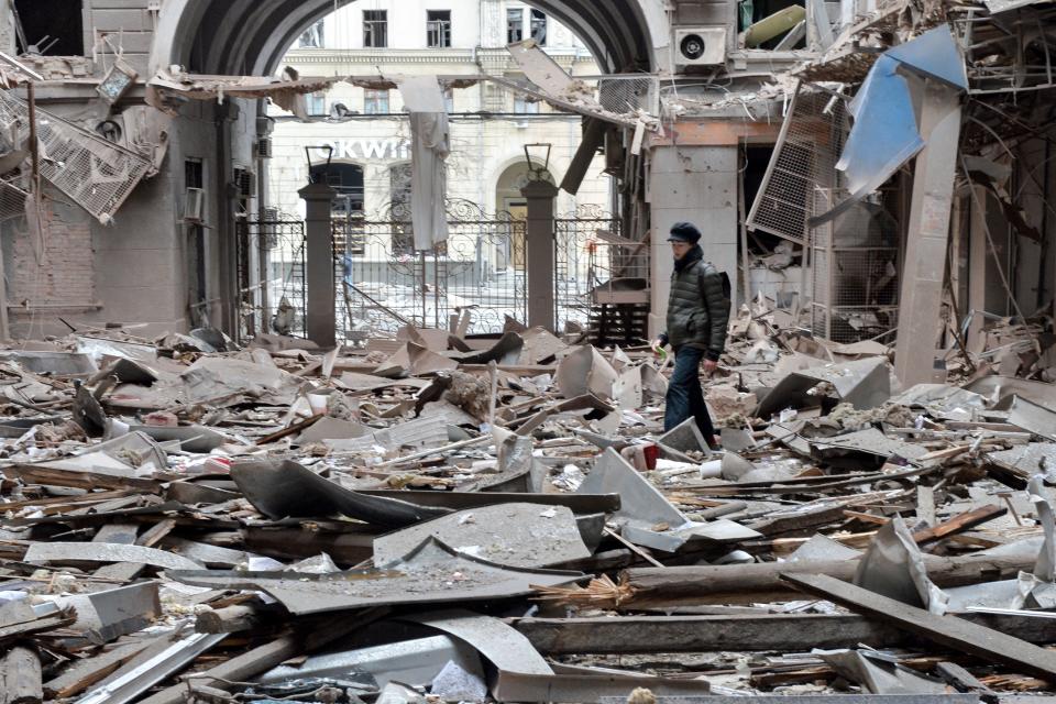 A view from inside of a heavily damaged building, with someone wearing all black standing amid the debris.