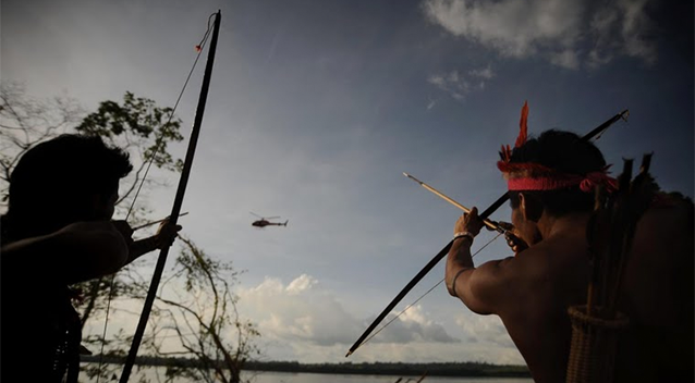 Munduruku indigenous people point their bows and arrows at a police helicopter flying over the barrier of the Belo Monte Dam's construction site in northern Brazil.  15 JUN 2012. ALTAMIRA, BRAZIL. REUTERS/LUNAE PARRACHO