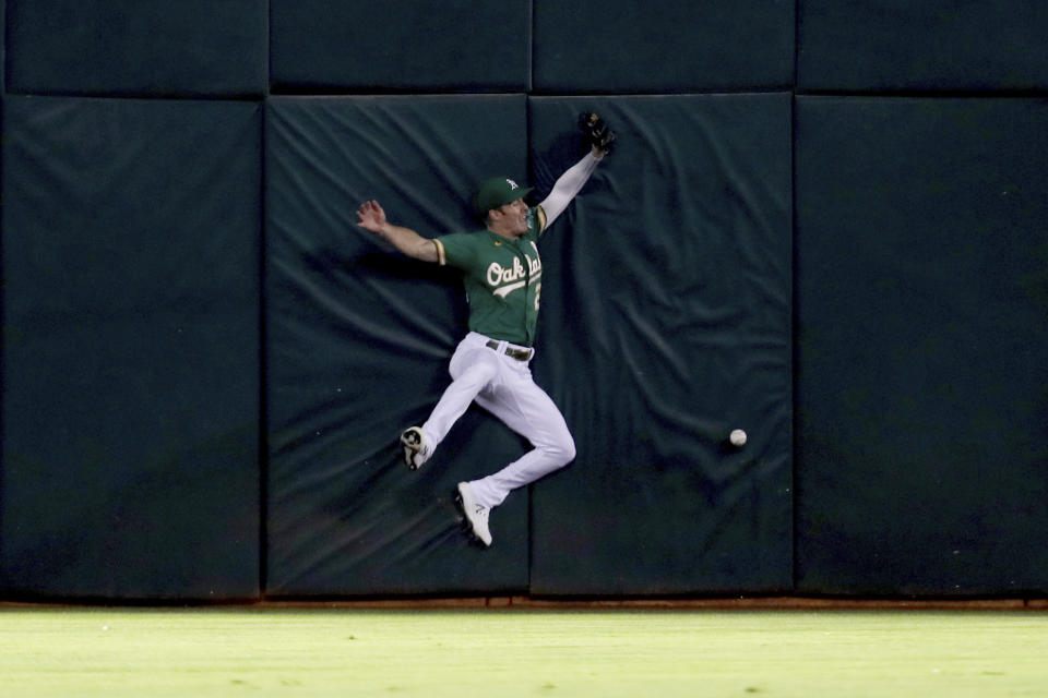 Oakland Athletics' Mark Canha crashes into the outfield wall on a triple hit by Seattle Mariners' Dylan Moore during the fourth inning of a baseball game in Oakland, Calif., Tuesday, Sept. 21, 2021. (AP Photo/Jed Jacobsohn)