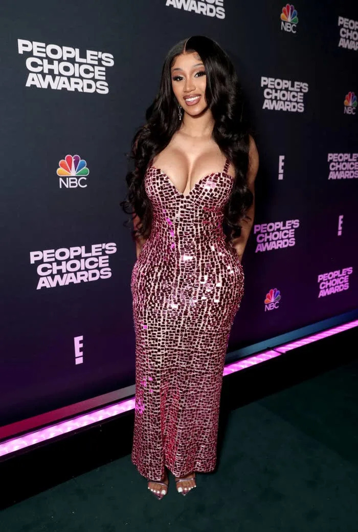 Cardi posing on the red carpet of the People's Choice Awards in a sequined dress with a sweetheart neckline