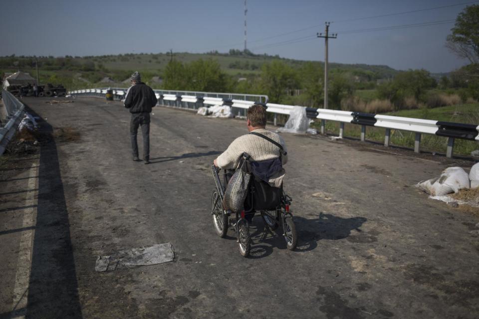 A disabled person goes over the bridge on a wheelchair at a pro-Russian insurgent checkpoint that has been used to block access to a road leading to Slovyansk, eastern Ukraine, Saturday, May 3, 2014. Local nearby residents say Ukrainian government troops opened fire on a crowd of unarmed protesters on this spot, where discarded shells and pools of blood could be seen. (AP Photo/Alexander Zemlianichenko)