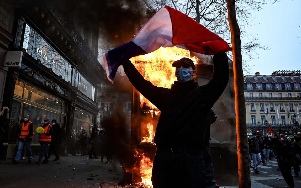 A protester holds a French flag next to a burning news kiosk beside the Place de l'Opéra - Alain Jocard/AFP/Getty Images