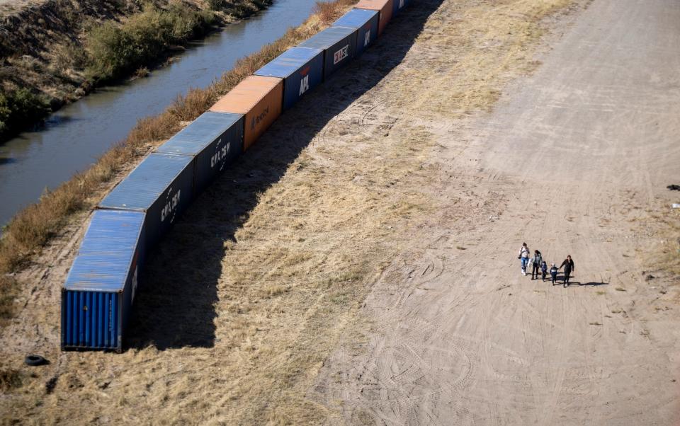 Migrants walk on along shipping containers that are being used as a makeshift border wall along the U.S.-Mexico border near Downtown El Paso on Saturday.