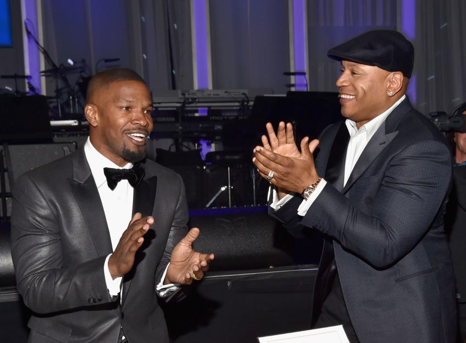 jaime foxx and ll cool j, both wearing black suits, clap and laugh