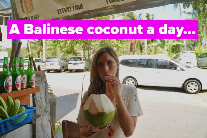 A woman drinking a coconut on the side of the road.