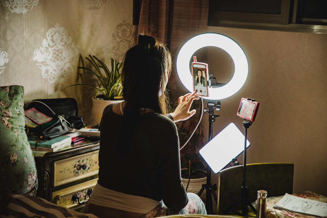 asian female influencer filming content using phone in a bedroom