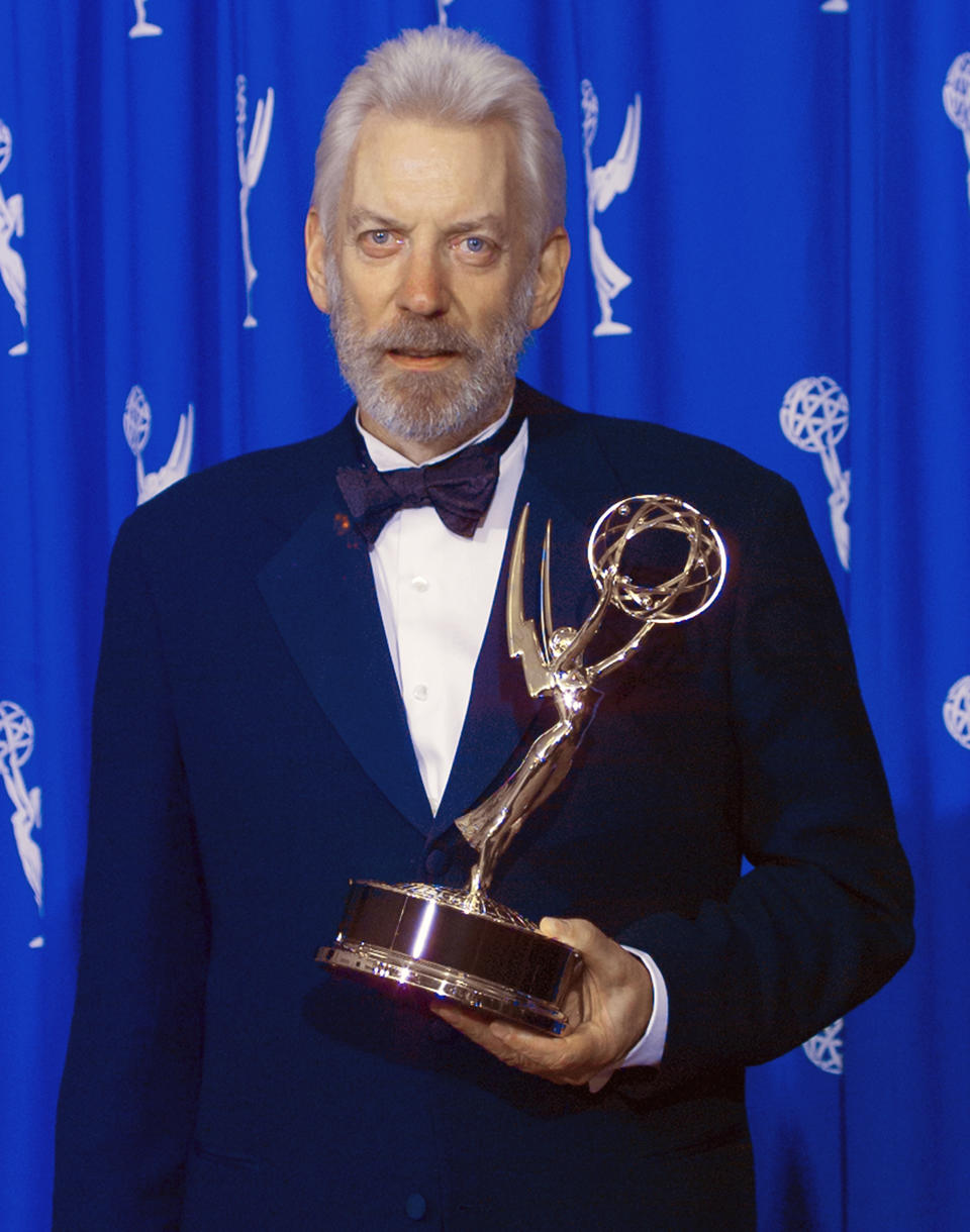 Donald Sutherland in a formal suit holding his Emmy Award  with Emmy logos