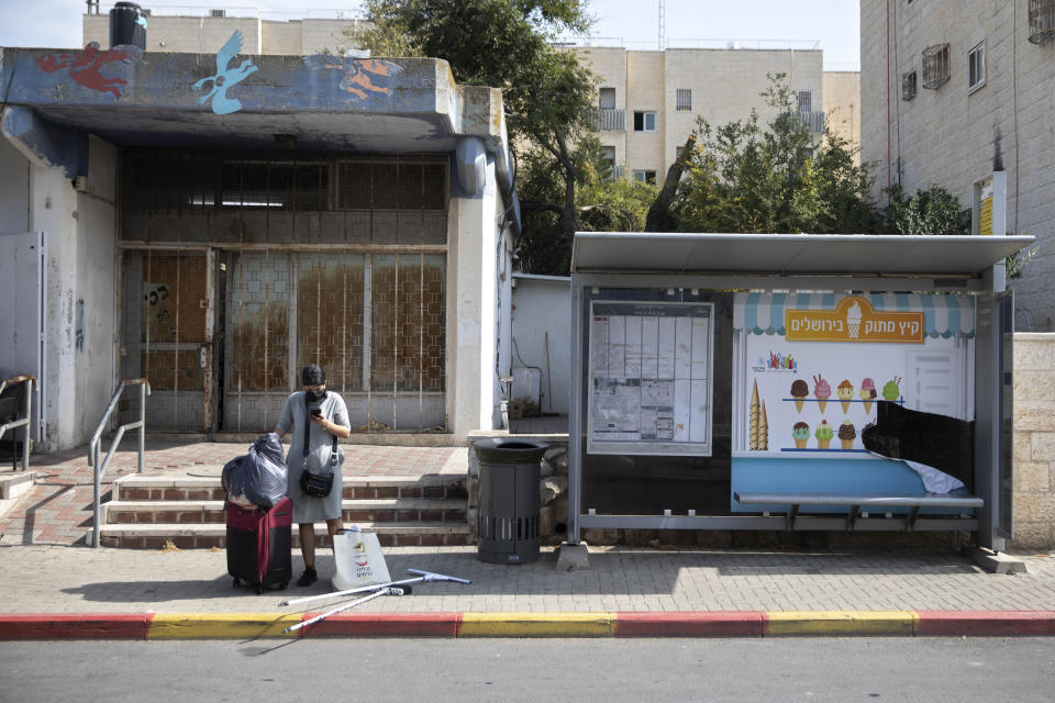 An Israeli woman waits for a bus near a trashcan installed next to a bus stop that applauds to those who use it, in Jerusalem, Thursday, Oct. 14, 2021. Drop a piece of trash in, and a recording of a child's voice says "Thank you very much!". (AP Photo/Sebastian Scheiner)