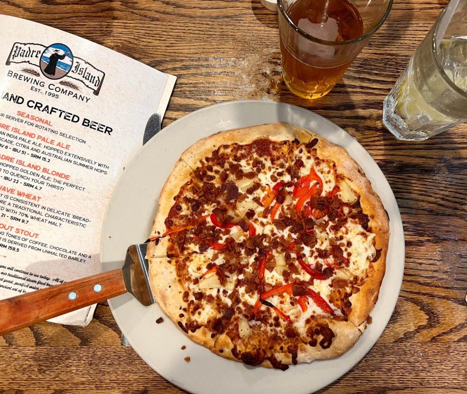 plate of pizza sitting on a wooden table with a craft beer and menu