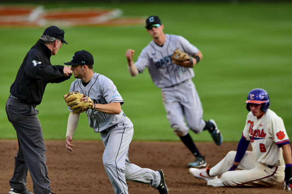 FILE - In this Wednesday, March 13, 2019, file photo, Coastal Carolina's Cory Wood, left, and Scott McKeon, center, react after tagging Clemson's Logan Davidson, right, out at second base during an NCAA college baseball game, in Clemson, S.C. Coastal Carolina already had a small athletic budget, and that was before a 15% spending cut was ordered because of projected declines in state funding and student fees stemming from the coronavirus pandemic. The school's 19-sport program includes about 450 athletes, and with individual tests currently costing about $100, testing could cost hundreds of thousands of dollars by the end of the 2020-21 academic year. (AP Photo/Richard Shiro, File)