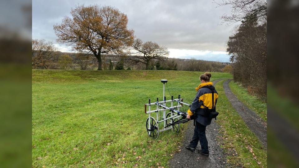 Here we see a person in a grassy field pushing a white contraption on 2 wheels.