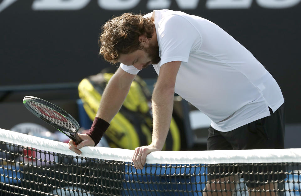 Latvia's Ernests Gulbis rests on the net, defeating Canada's Felix Auger-Aliassime in their first round singles match at the Australian Open tennis championship in Melbourne, Australia, Tuesday, Jan. 21, 2020. (AP Photo/Dita Alangkara)