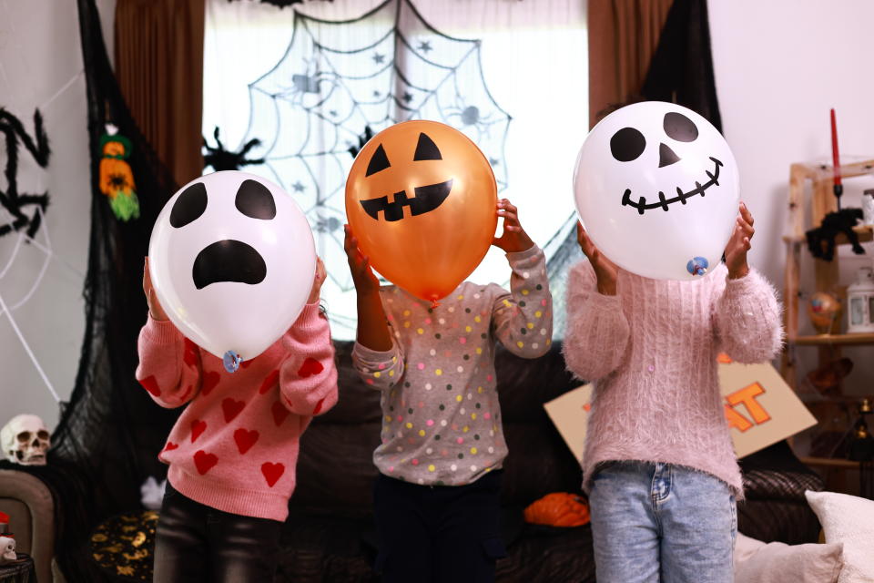 group of children holding a balloon they drew a ghost on, in front of their face finances