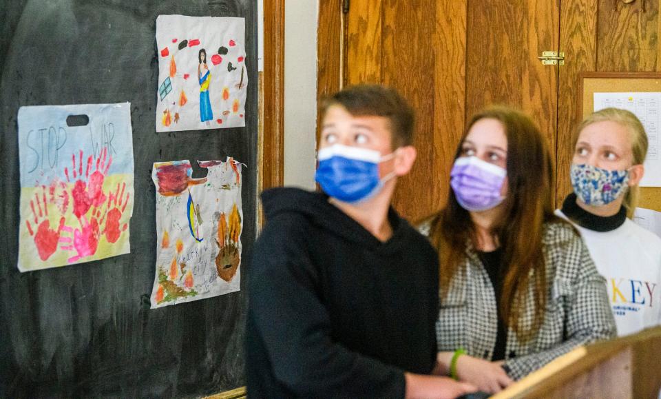 Artwork created by Ivan Kovalyov, left, Zlata Yadukha, middle, and Violetta Pryschepova hangs behind the youth as they look at images from Russia's war on Ukraine during a presentation at Harmony School on Tuesday, May 24, 2022.