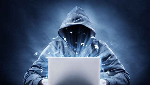 Hooded figure typing on laptop