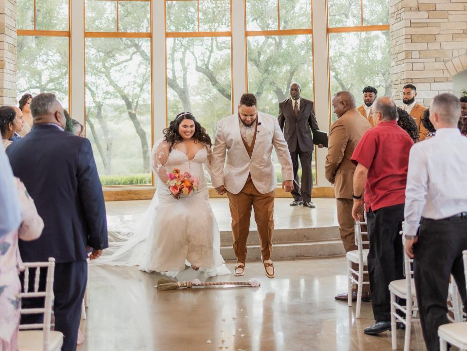 A bride and groom jump the broom as they exit their wedding ceremony.