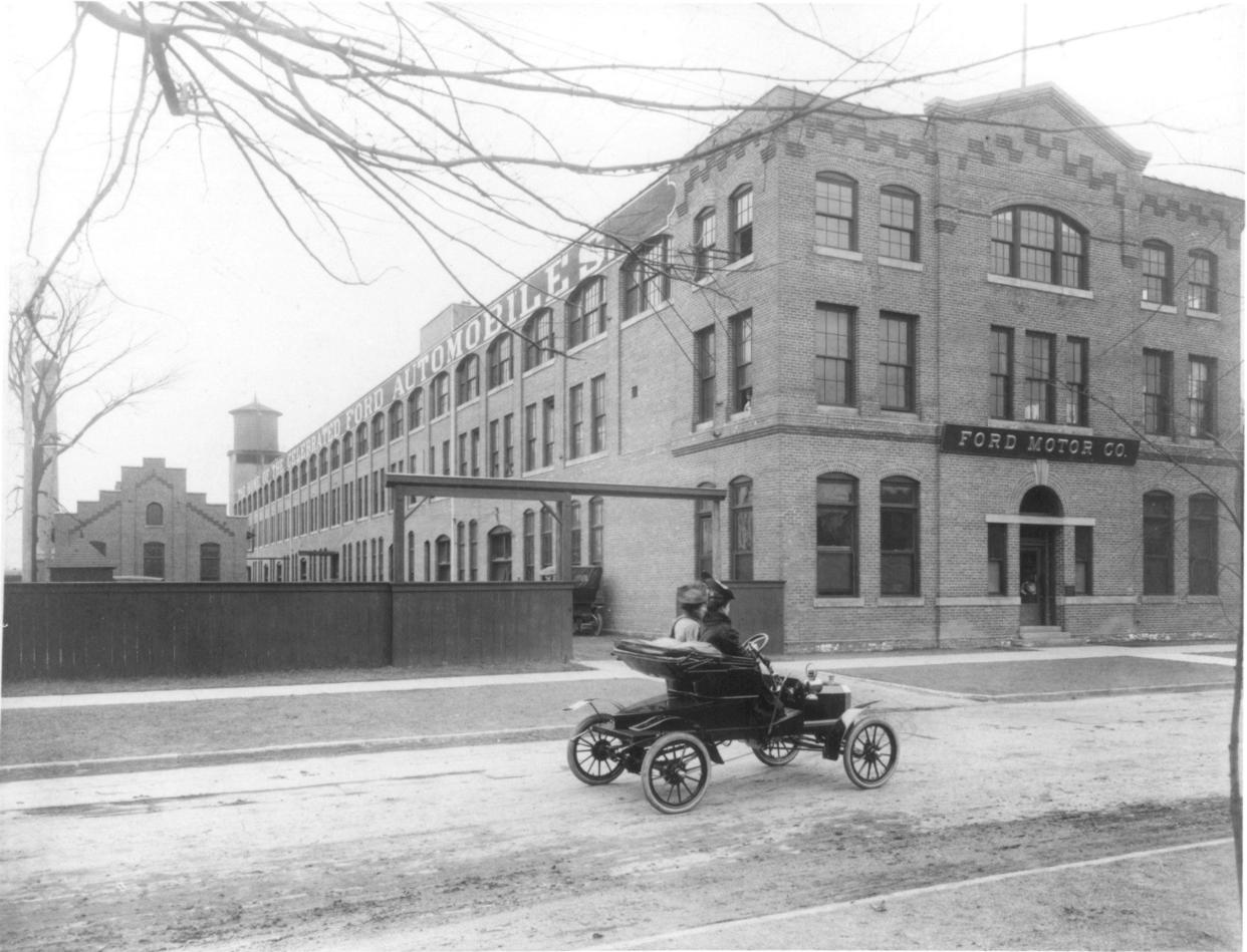 Clara Ford, right, drives a 1905 Model N with Merle Clarkson in front of the three-story brick factory shown in 1905 that from late 1904 to 1910 was the home of Ford Motor Co.