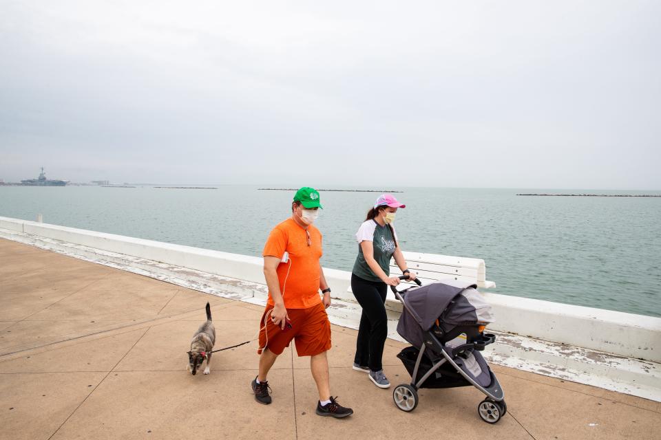 People wearing face masks walk along the seawall on North Shoreline Boulevard in Corpus Christi, Texas, on Monday.