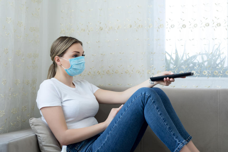 Quarantined woman wearing protective mask watching tv in the living room