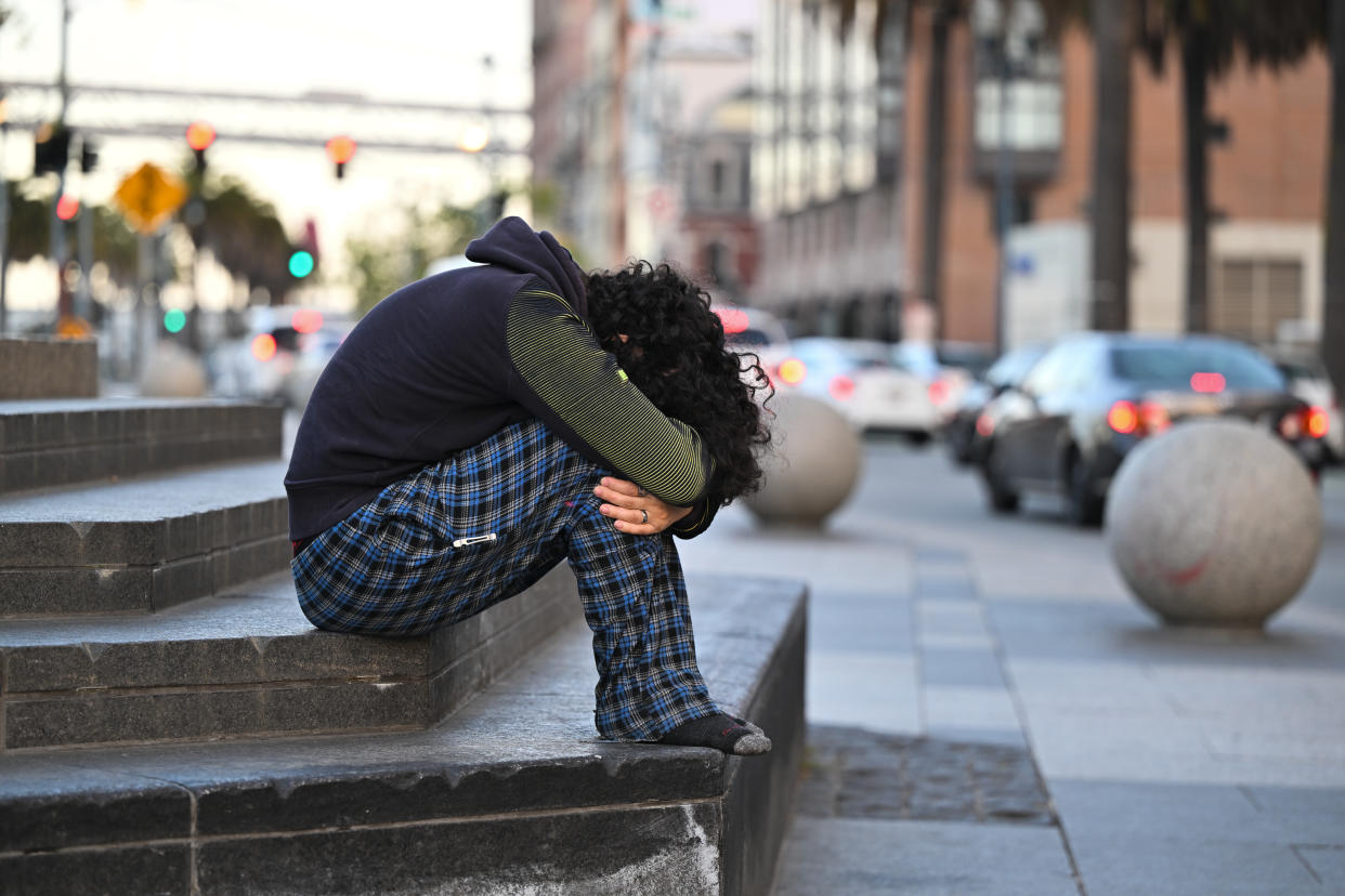 A person with curly hair, face buried in their lap, sits hunched on some steps.