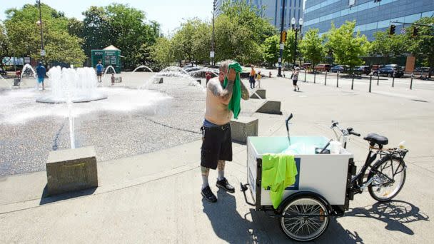 PHOTO: Matthew Carr dries himself after cooling off in the Salmon Street Springs fountain before returning work cleaning up trash on his bicycle in Portland, Ore., July 26, 2022 (Craig Mitchelldyer/AP)