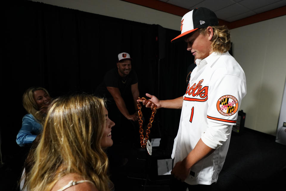CORRECTS DATE - Jackson Holliday, right, the first overall draft pick by the Baltimore Orioles in the 2022 draft, holds an Orioles home run chain during a news conference introducing him to the Baltimore media prior to a baseball game between the Baltimore Orioles and the Tampa Bay Rays, Wednesday, July 27, 2022, in Baltimore. Looking on are Holliday's parents, former major league player Matt Holliday, center, and Leslee Holliday, left, as well as Holliday's girlfriend Chloe Cox, bottom left. (AP Photo/Julio Cortez)